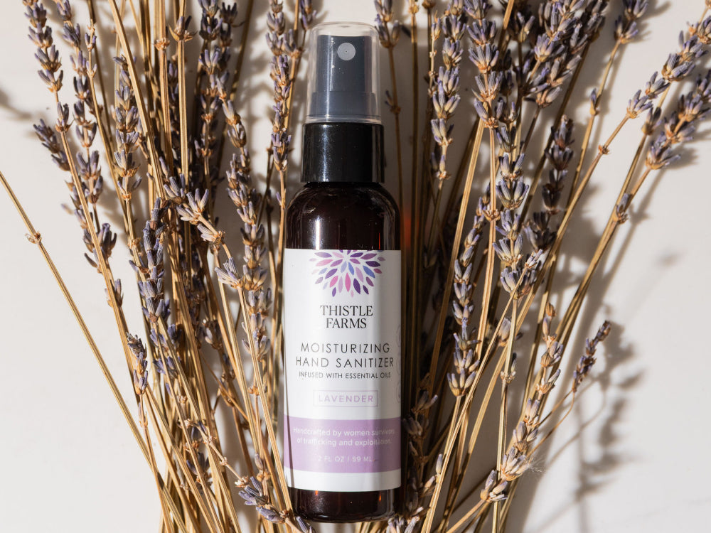 Bottle of Thistle Farms hand sanitizer surrounded by lavender flowers on a light background