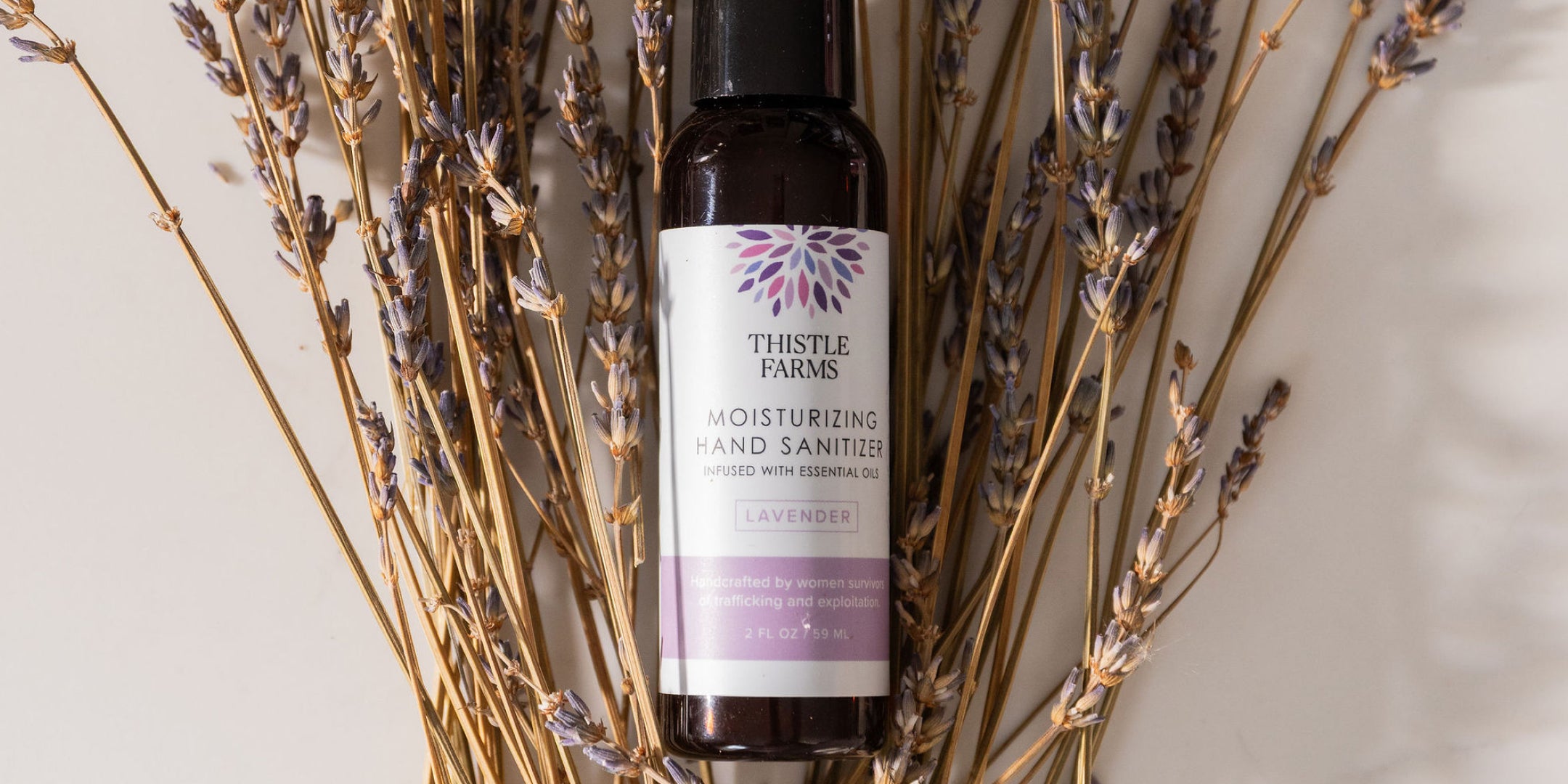 Thistle Farms hand sanitizer bottle surrounded by lavender flowers on a neutral background