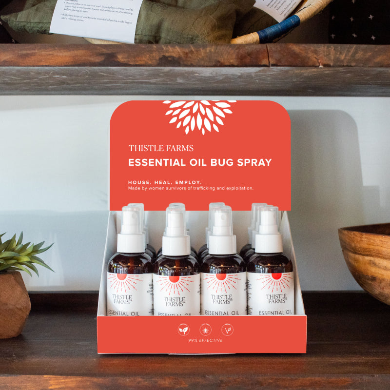 Essential oil bug spray packaging on a wooden shelf with decorative items.