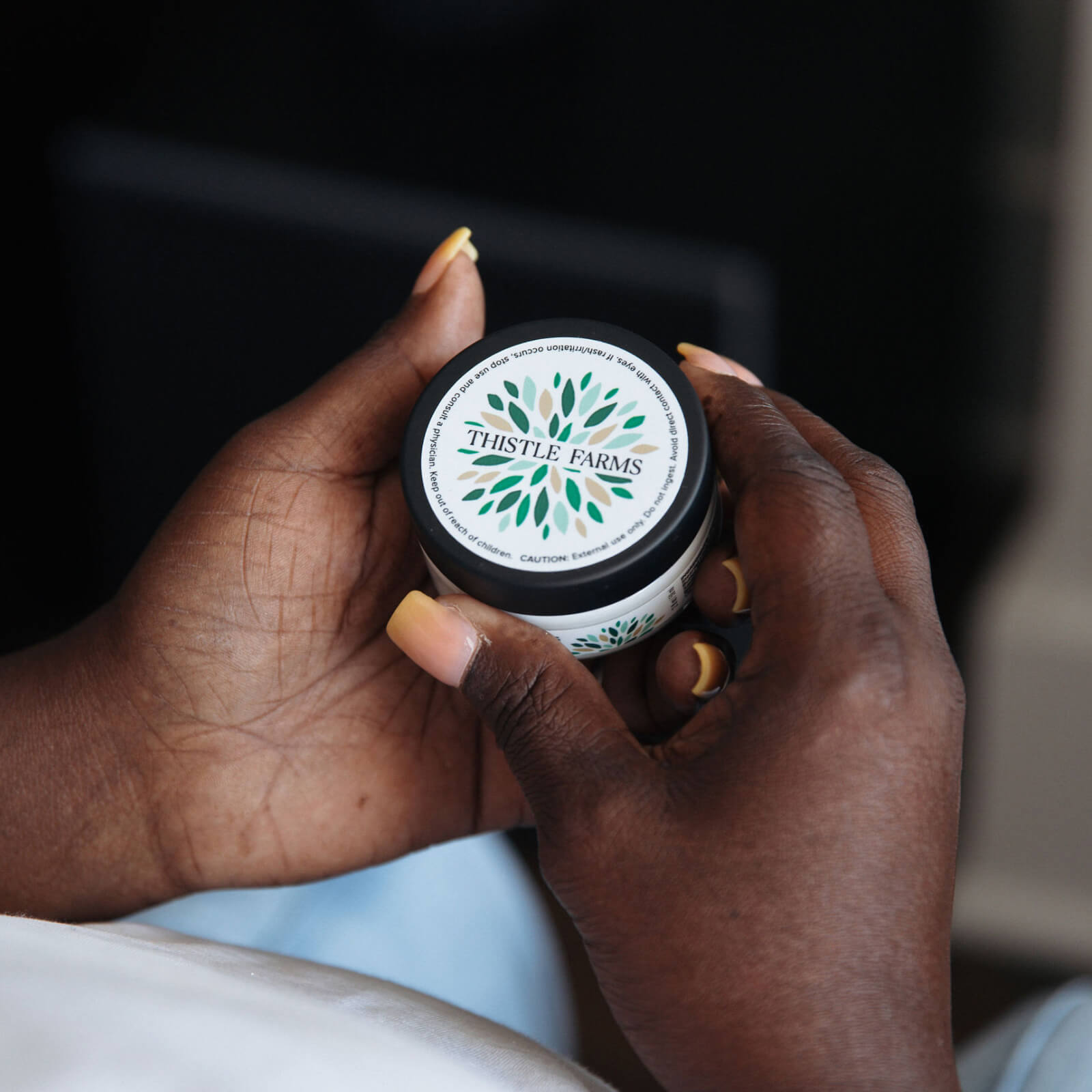 Hand holding a jar of body butter against a blurred background