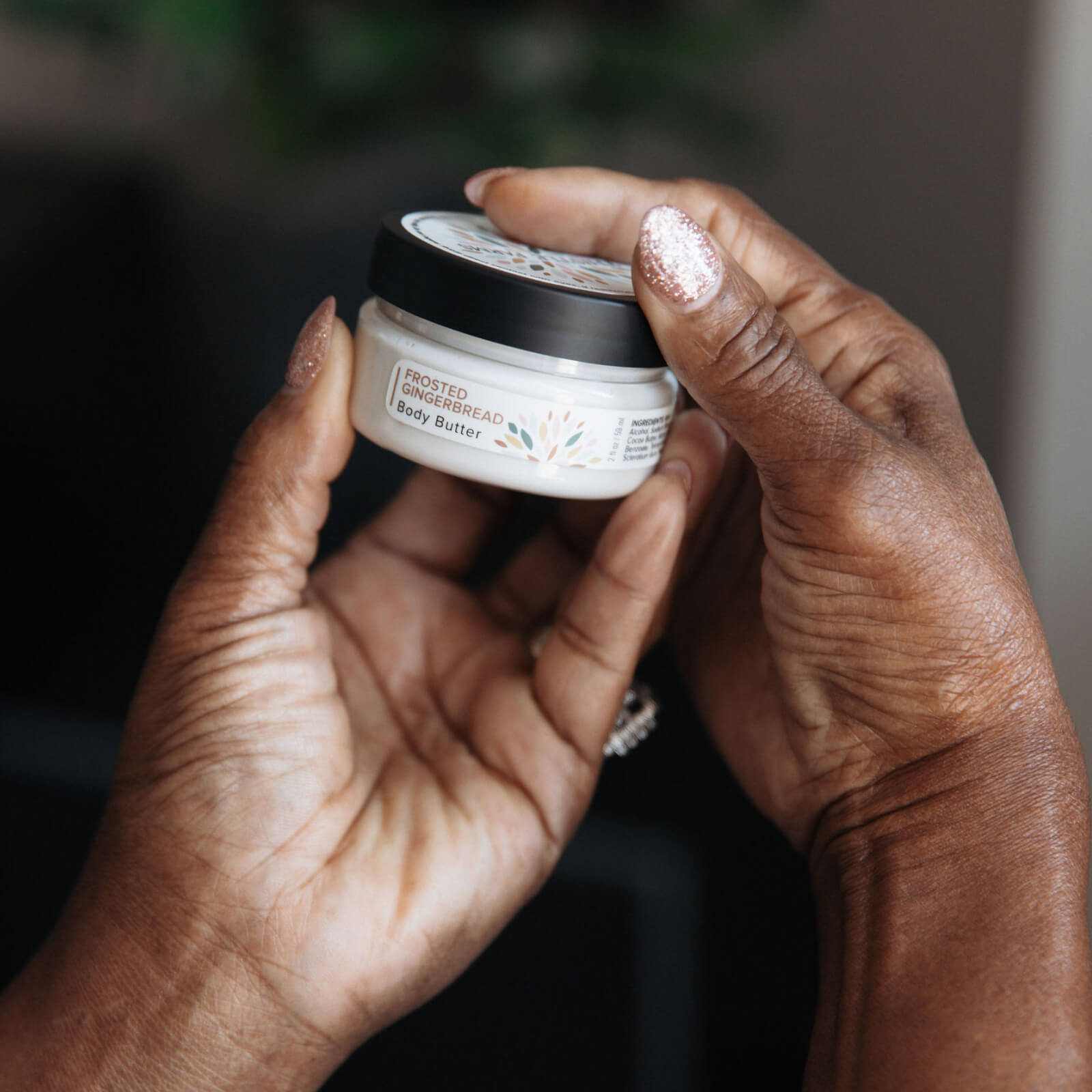 Two hands holding a jar of body butter against a blurred background