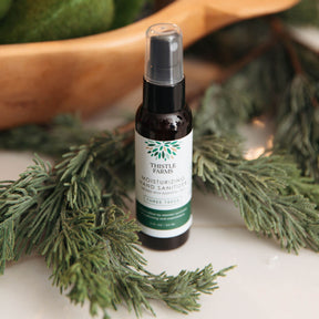 Thistle Farms hand sanitizer bottle surrounded by greenery on a white surface