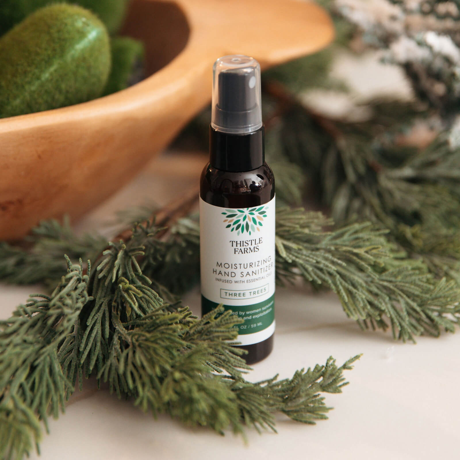 Thistle Farms hand sanitizer bottle surrounded by greenery on a white surface