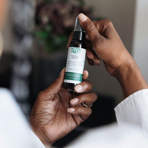Person holding a bottle of Thistle Farm hand sanitizer with a blurred background