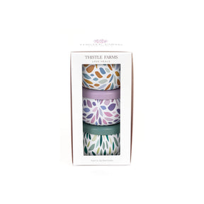 Three patterned candles in a box with 'Thistle Farms' branding on a white background