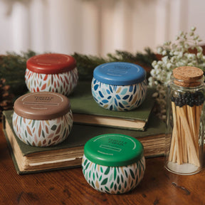 Set of small jars with patterned lids on books, surrounded by a glass container with matches and decorative elements.