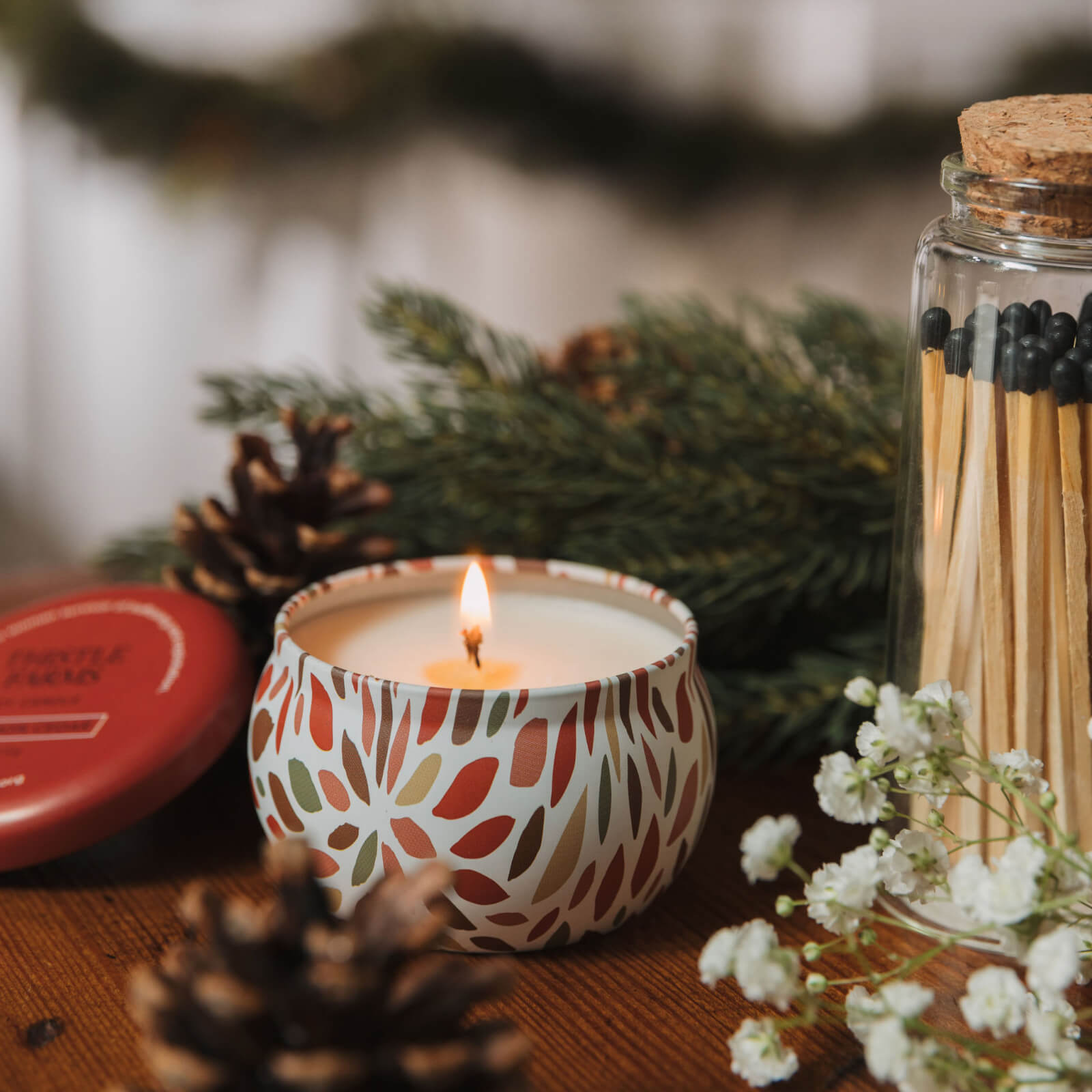 Candle with decorative pattern, matches, and greenery on a wooden surface