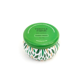 Thistle Farms soy candle with a green lid and a patterned base on a white background