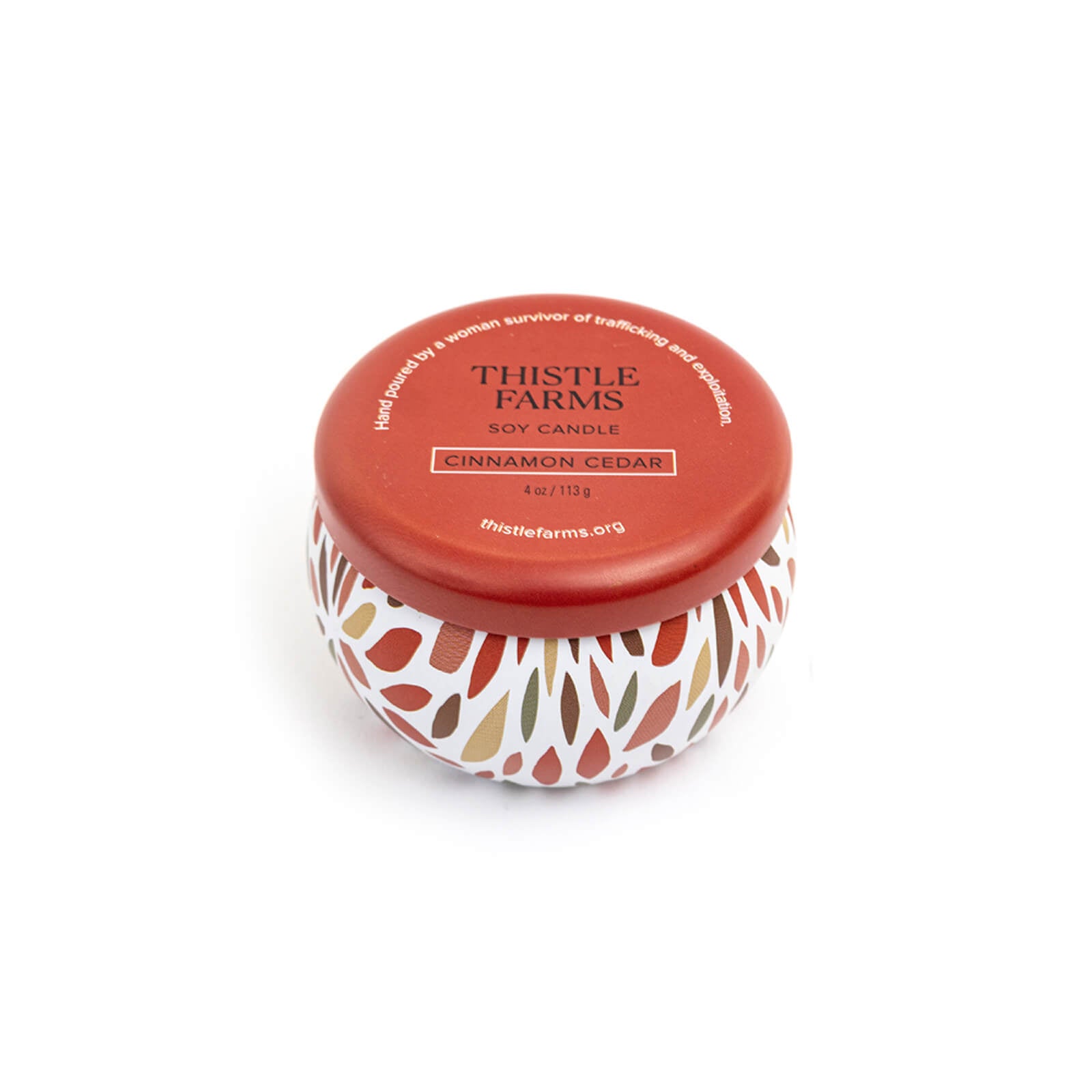 Thistle Farms soy candle with a red lid and a patterned base on a white background