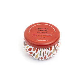 Thistle Farms soy candle with a red lid and a patterned base on a white background