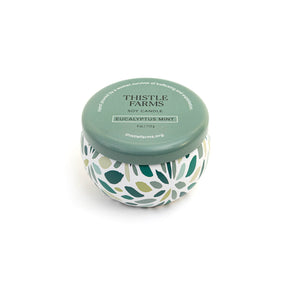 Thistle Farms soy candle with a green lid and a patterned base on a white background