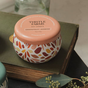 Thistle Farms soy candle with an orange lid on a book