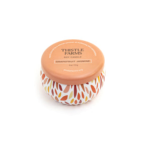 Thistle Farms soy candle with an orange lid and a patterned base on a white background
