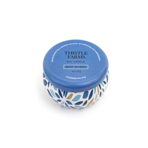 Thistle Farms soy candle with a blue lid and a patterned base on a white background