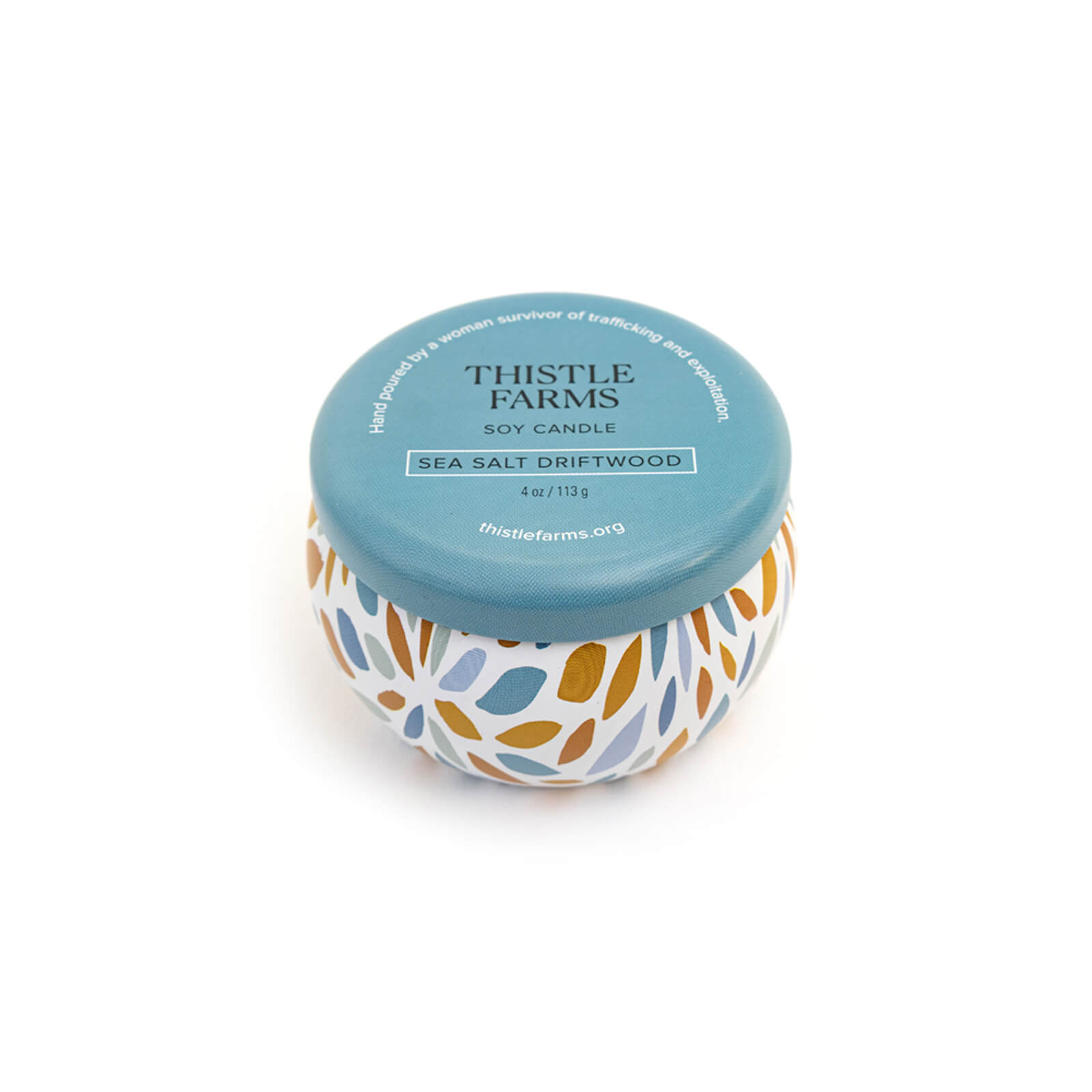Thistle Farms soy candle with a blue lid and a patterned base on a white background