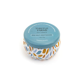 Thistle Farms soy candle with a blue lid and a patterned base on a white background