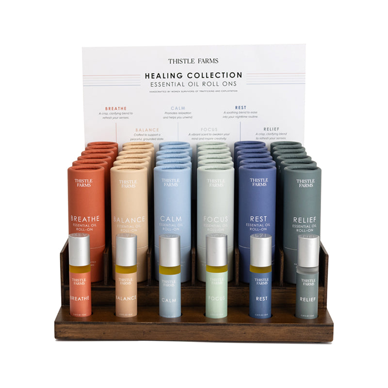 Thistle Farms Healing Oil Collection with various colored bottles on a wooden stand.